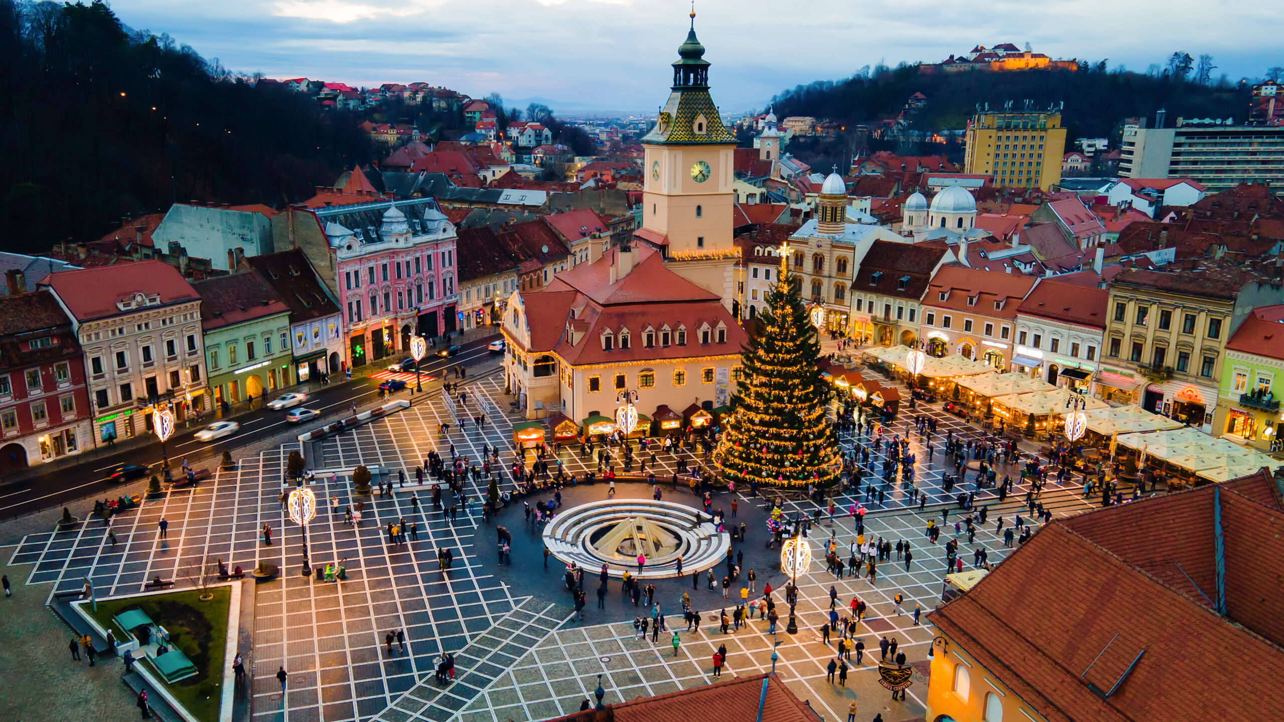 Aerial drone view of The Council Square at dusk in Brasov, Romania. Old city centre decorated for Christmas. County Museum of History, buildings, people